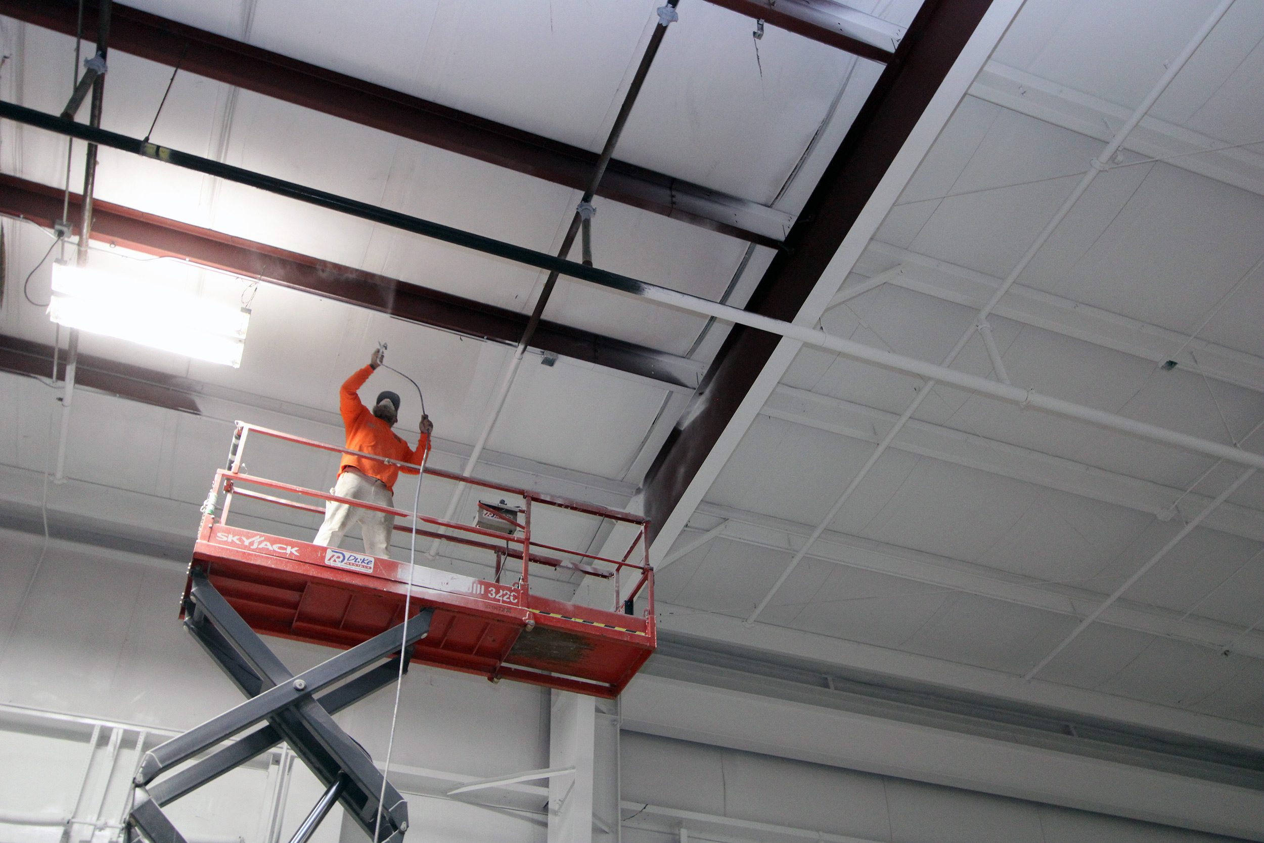 A JC Toland employee sprays intumescent sealant on a ceiling